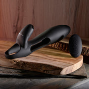 A sleek, black Nautilus Rechargeable Vibrating Penis Sleeve for Couples with Remote Control rests on a wooden slab, its elegant design accentuated by a textured natural wood backdrop.