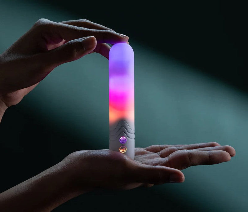 Hands holding a white, sleek bullet vibrator glowing with purple, pink, and orange LED lights.
