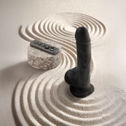 Black realistic rotating vibrating dildo with remote control on raked sand.