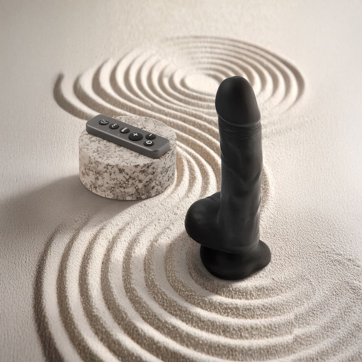 Black realistic rotating vibrating dildo with remote control on raked sand.
