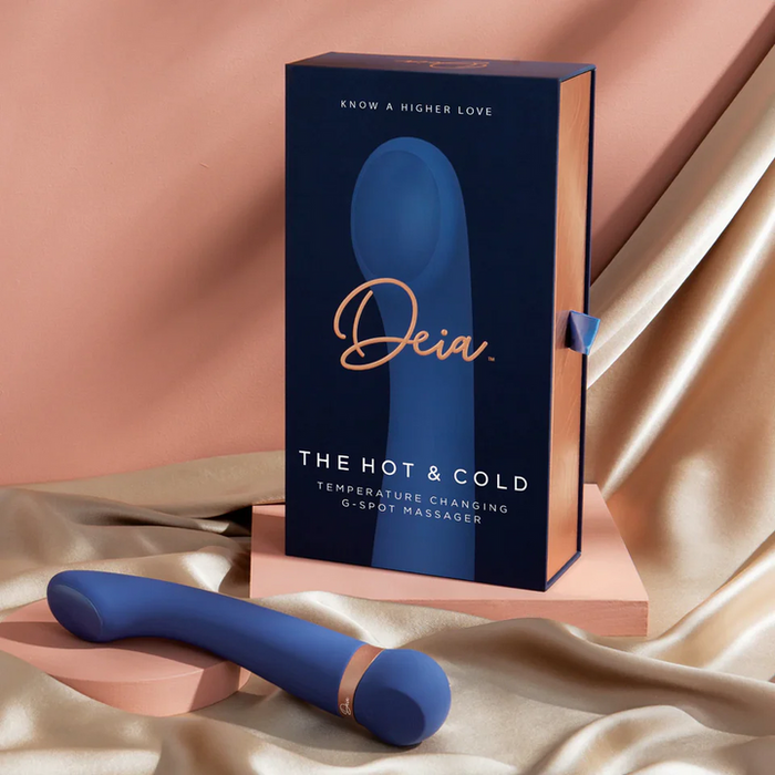 A blue Hot & Cold Temperature-Changing G-Spot Massager sits in front of its box, with soft pink fabric and platforms highlighting this unique temperature play toy.