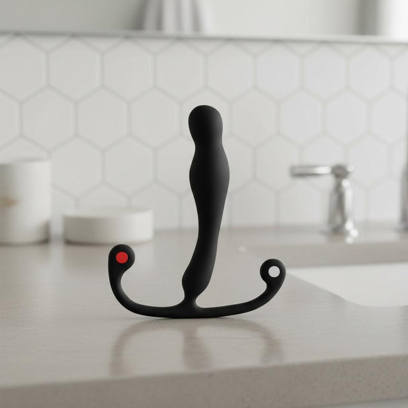 The Aneros Eupho Syn Trident Hands-Free Prostate Stimulator is black with a curved design and two rounded handles—one marked red, one white—set against a light gray background, ideal for targeted prostate stimulation.