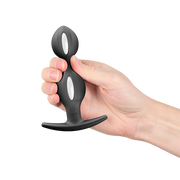 Hand holding a black silicone butt plug with white weighted inner balls and a flared base.