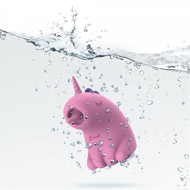 The Dreamy Licks – The Whimsical Unicorn Tongue Vibrator is a pink, cartoon-inspired unicorn made of body-safe silicone with a purple horn and closed eyes, pictured underwater with bubbles and splashes on a white background.