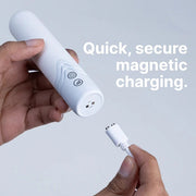 Hand holding a white bullet vibrator with magnetic charging port and a white magnetic USB cable.