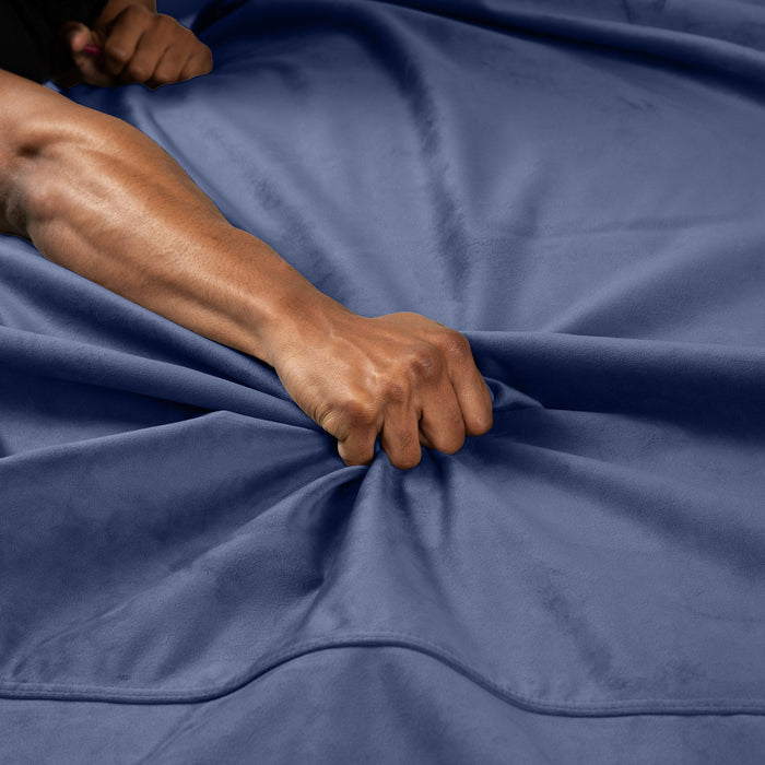 A person’s hand grips and bunches up the soft blue Liberator Fascinator Throw Velvety Waterproof Sex Blanket, creating folds and wrinkles in the fabric.