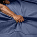 A person’s hand grips and bunches up the soft blue Liberator Fascinator Throw Velvety Waterproof Sex Blanket, creating folds and wrinkles in the fabric.