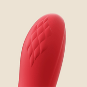 Close-up of the tip of the Fortexa Kinky Finger Rabbit Vibrator with App Control, featuring red silicone and a diamond-textured pattern against a plain, light beige background.