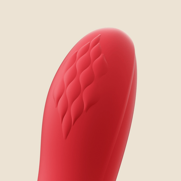 Close-up of the tip of the Fortexa Kinky Finger Rabbit Vibrator with App Control, featuring red silicone and a diamond-textured pattern against a plain, light beige background.