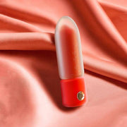 Red lipstick vibrator with a frosted translucent cap and gold button, on a silky pink fabric.