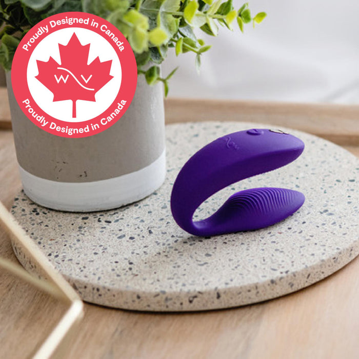 A purple We-Vibe Sync 2 Wearable Couples Vibrator – Remote and App Controlled – rests on a speckled tray beside a white planter with green leaves. A red maple leaf logo announces, "Proudly Designed in Canada.