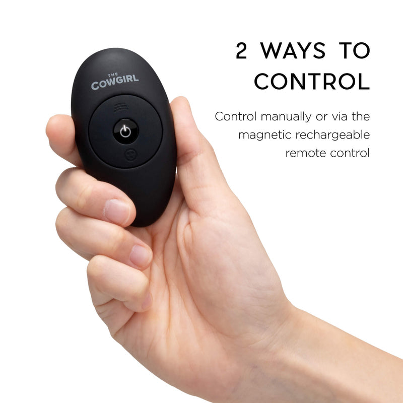 A hand holds a black oval remote labeled "The Cowgirl." Text reads: "Control The Cowgirl Saddle Sex Machine with Vibration, Thrusting & Rocking manually or via the magnetic rechargeable remote for seamless, hands-free pleasure.