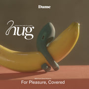 A green silicone Dame Hug Adjustable Vibrating Cock Ring for Couples, designed to wrap around a banana, sits on an orange surface. The text reads "hug," "Dame," and "For Pleasure, Covered. NEW adjustable cock ring from Dame Products.