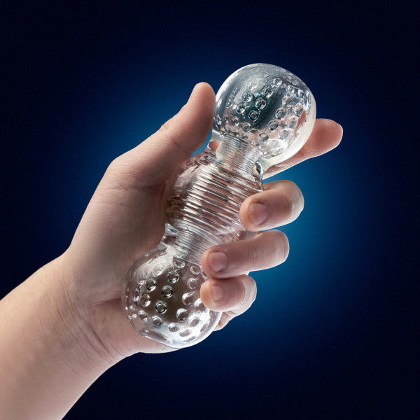 A hand holds the Rize Feelz Clear Textured Stroker, a transparent reversible male masturbator with bumpy surfaces and a ribbed center, displayed against a dark blue background.