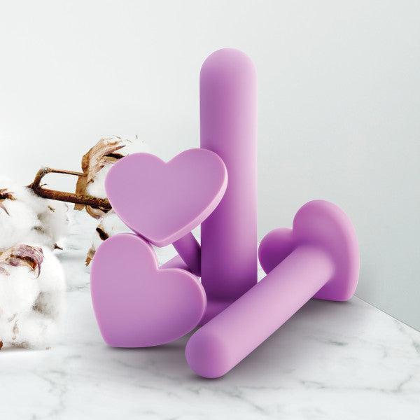 A set of Blush Wellness Vaginal Dilator Kit Graduated Set of 4 with heart-shaped bases is arranged on a white marble surface. Cotton branches in the background add a soft, natural element to the scene, highlighting the body-safe silicone material.